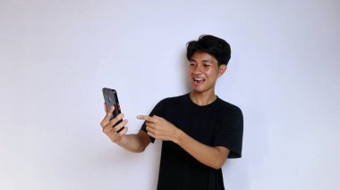 Siyah tişörtlü genç Asyalı adam izole edilmiş beyaz arka planda akıllı telefon tutuyor ve bakıyor.