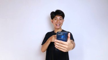 Siyah tişört giyen mutlu Asyalı genç adam izole edilmiş beyaz arka planda akıllı telefon kamerasıyla selfie çekiyor.