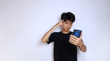 Siyah tişörtlü genç Asyalı adam izole edilmiş beyaz arka planda akıllı bir telefon düşünüyor.
