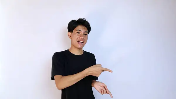 stock image excited young asian man wearing black shirt gesturing with hand pointing to the side on isolated white background. copy space