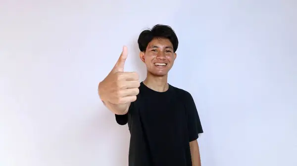 stock image Excited young Asian man wearing black shirt gesturing with thumb on hand on isolated white background. copy space, success, happiness, say yes, okay, good, delicious