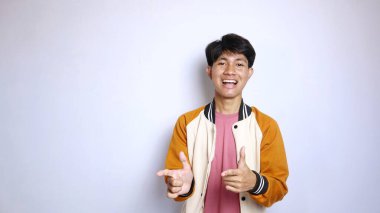 Sıradan gülümseyen, yakışıklı, ceketli Asyalı bir adam izole edilmiş beyaz arka planda bir tarafı işaret ediyor.