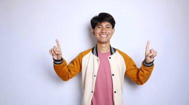 Sıradan gülümseyen, yakışıklı, ceketli Asyalı bir adam soyutlanmış beyaz arka planda yukarı doğru hareketler yapıyor.