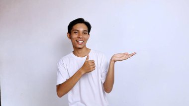 Young Asian man in white shirt smiling gesture showing thumbs up towards palm isolated white background, copy space clipart