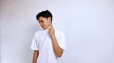 Beyaz gömlek giyen genç Asyalı adam gömleğinden kötü bir koku alıyor. İzole edilmiş beyaz arka plan, kopyalama alanı.