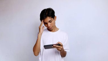 Asyalı genç adamın başı dönüyor beyaz gömlekli, cep telefonuyla oyun oynuyor. Oyunda kayboldum