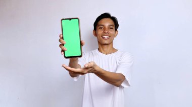 Beyaz tişörtlü gülümseyen Asyalı genç adam reklam için yeşil ekranlı cep telefonunu gösteriyordu. yaşam tarzı konsepti