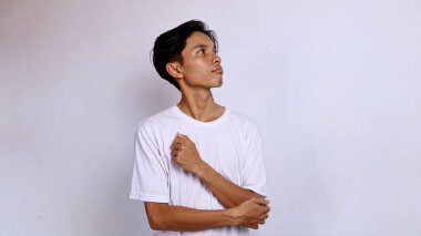 Beyaz tişörtlü genç Asyalı adam beyaz arka planı olan bir şey düşünüyor.