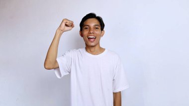 İki elini de sıkarak heyecanlanan Asyalı genç adam mutlu, mutlu, kazanan, kutlayan izole beyaz arka plan.