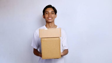 Asyalı genç adam beyaz gömlek içinde gülümsüyor. Elinde beyaz arka planda bir paket kutusu var.