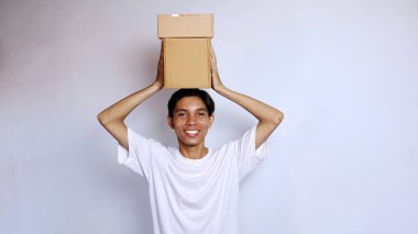 Asyalı genç adam gülümsüyor, beyaz gömlek giyiyor, kafasının üstünde beyaz arka planı olan bir paket kutusu var.