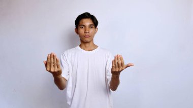 Asyalı genç adam beyaz gömlekli, elleri öne bakacak şekilde hareket ediyor.