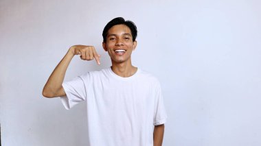 Beyaz gömlekli genç Asyalı adam izole edilmiş beyaz arkaplanı işaret ederken gülümsüyor, boşluğu kopyala