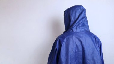 İzole edilmiş beyaz arka planda yağmurluk giyen Asyalı genç bir adam.