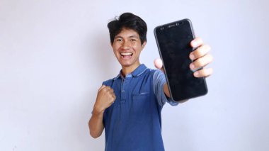 Mutlu Asyalı genç adam beyaz arka planda akıllı telefon tutuyor ve gösteriyor.