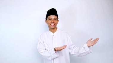 Yakışıklı Asyalı genç Müslüman adam gülümsüyor elini gösteriyor beyaz arka planda izole edilmiş bir şey tavsiye ediyor.