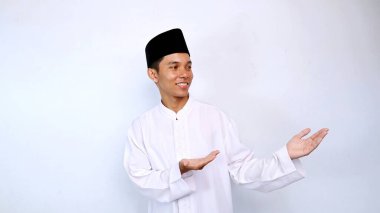 Yakışıklı, Asyalı, gülümseyen, elini gösteren, beyaz arka planda izole edilmiş bir şey öneren Müslüman bir adam.