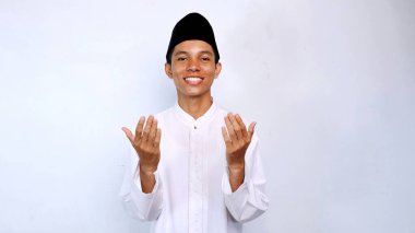 Yakışıklı Asyalı Müslüman gençlik gülümseyen, el hareketi yapan, izole edilmiş beyaz bir geçmişle dua eden.