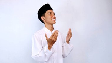 Yakışıklı Asyalı Müslüman genç adam el kaldırıyor ve beyaz arka planda dua ediyor.