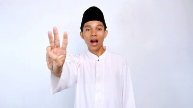 Yakışıklı Asyalı Müslüman genç adam üç numarayı gösteriyor. Parmaklarını izole edilmiş beyaz arka planda kullanıyor.