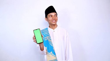 Yakışıklı Asyalı müslüman genç adam gülümsüyor. Yana bakıyor. Cep telefonu ekranı görünüyor.