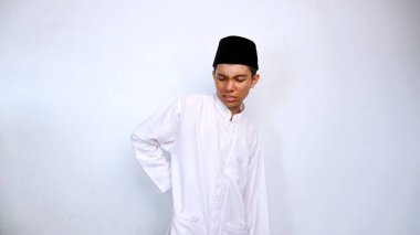 Genç Asyalı Müslüman erkek, izole edilmiş beyaz arka planla bel bölgesinde acı içinde el kol hareketi yapar.