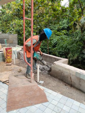 a worker is dismantling a concrete wall with a jack hammer. Bali - Indonesia ; December 14, 2022.