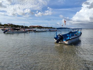 several boats parked on the beach, visible white clouds and clear blue sky.
