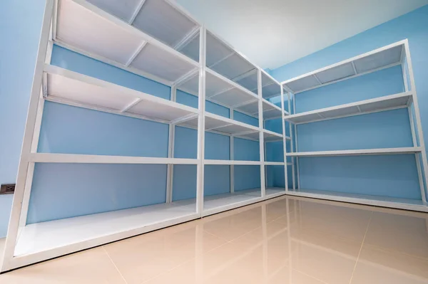 Empty white shelves in blue storage room, Thailand.