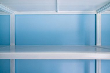 Empty white shelves in blue storage room, Thailand.