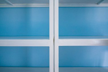 Empty white shelves in blue storage room, Thailand.