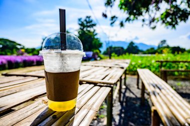 Fresh ice tea in plastic glass with flower garden, Chiang Mai province.