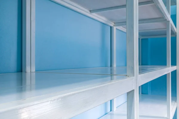 Empty white shelves in blue storage room, focus at front shelf