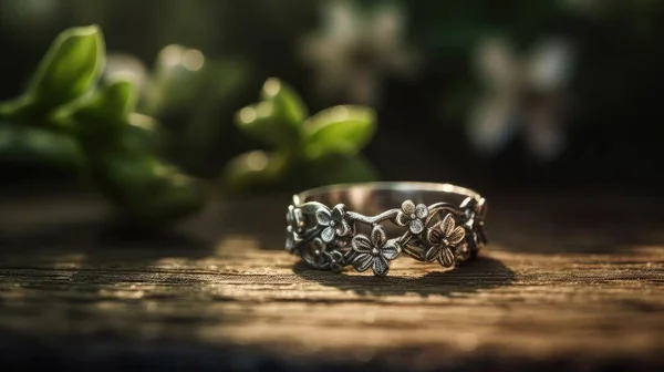A close-up photograph of a delicate silver ring on a finger, adorned with a small flower ornament. The ring has a simple band with a smooth, shiny finish, and the small flower is intricately crafted with fine details.