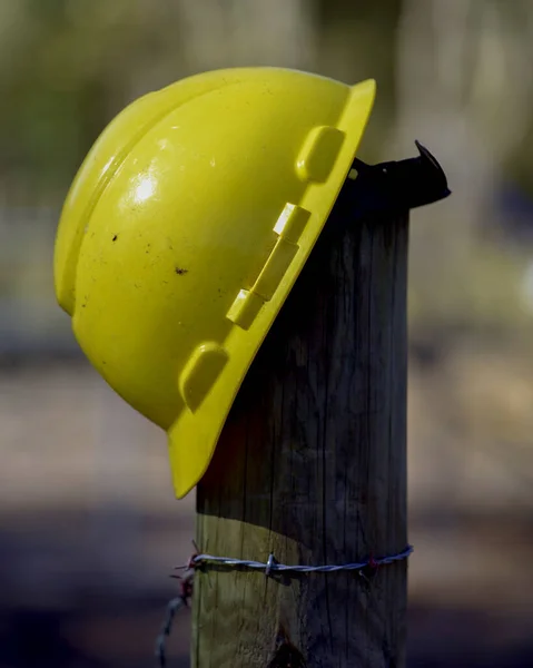 A yellow construction workers helmet on a fence post