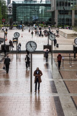 Commuters walking through Reuters Plaza, Canary Wharf, London. Six Public Clocks by Konstantin Grcic.