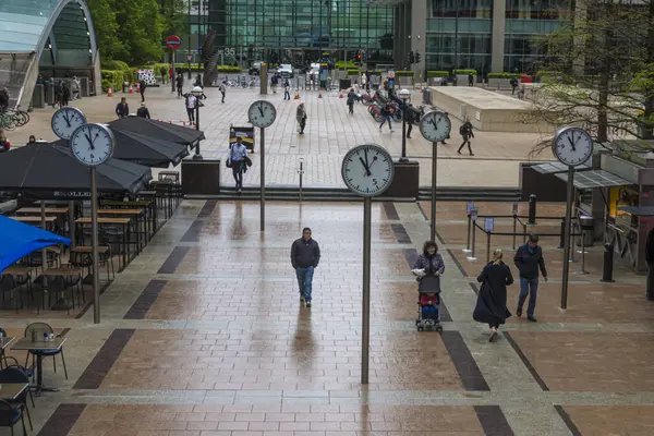 Commuters walking through Reuters Plaza, Canary Wharf, London. Six Public Clocks by Konstantin Grcic.