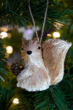 Squirrel Christmas ornament sitting in an artificial Christmas tree with Christmas light in background