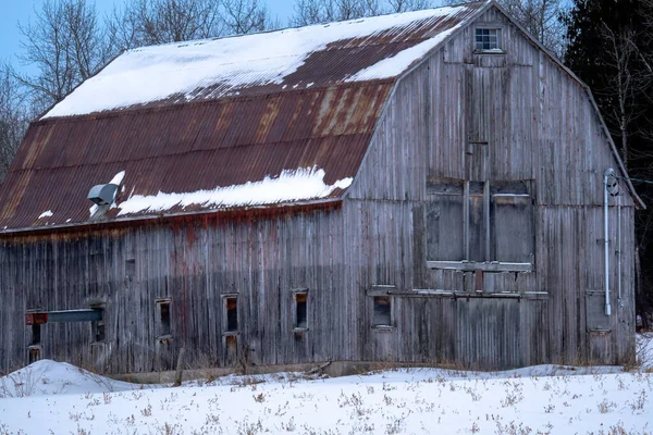 An old barn in the winter with snow on it\'s rusted tin roof