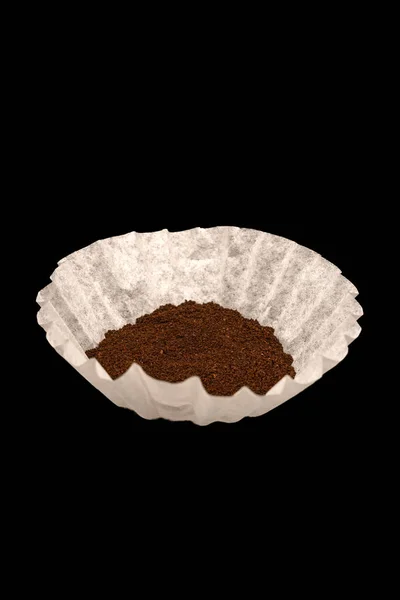 Coffee grounds in a white coffee filter on black background.
