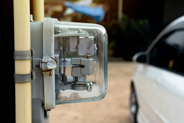 Front view of Power meter of Thailand attached to outdoor power pole. with yellow pipe beside of volt meter. and blurred of car parking on the ground.