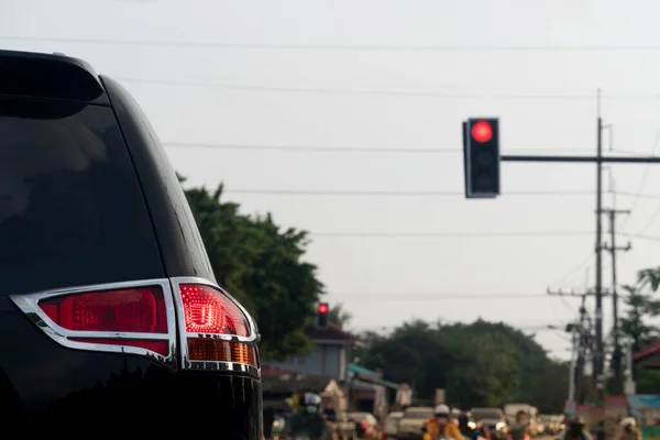 Rear side of black car with turn on brake light. Stop on the road by traffic light control red color. Environment of evening time. Blurred of cars and motorbikes parked lined up in the distance.