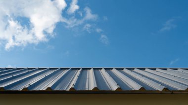 Çatıdaki mavi çatılı metal levha. Evin Hip Roof 'u çok güzel çizilmiş. Mavi gökyüzü ve beyaz bulutların altında bir ev inşa ediliyor..