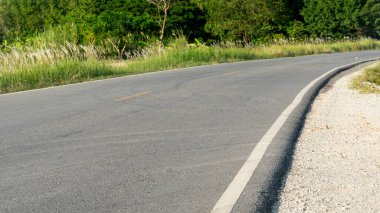 Asfalt yola doğru giden kıvrımlı bir yol. Yeşil çimenlerin ve ağaçların doğasının dışında.
