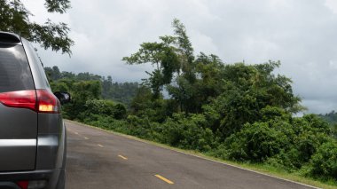 Asfalt yolda sarı çizgili gri arabanın arka tarafında. Dönüş sinyalini aç. Yeşil çim ve ormanın yanında. Nehirden bulanık. Chanthaburi 'den ziyade Khiri rezervuarı seyahati.