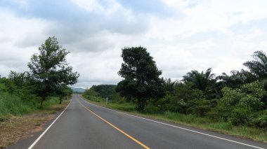 Asfalt yolun dikey yolu ve dümdüz devam ediyor. İki tane de yeşil çimenli ve ağaçlı orman. Mavi gökyüzü ve beyaz bulutların altında. Chanthaburi 'nin Ban Chokdee yolu.