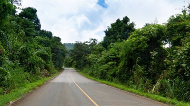 Asfalt yolun dikey yolu ve ilerideki kavis. İki tane de yeşil çimenli ve ağaçlı orman. Mavi gökyüzü ve beyaz bulutların altında. Khiri rezervuarına giden yol Chanthaburi 'den.