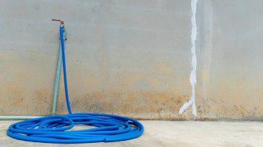 Mavi su hortumu musluk gövdesinin dışında bir daire şeklinde sarılmış. Beton zeminde ve beton duvarda. Evin yanında..