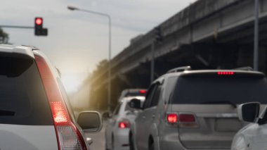 Arka taraftaki beyaz renkli araçlar yolculuğun amacına doğru ilerliyor. Gündüz trafiği yoğun. Kenarda bir köprü var..