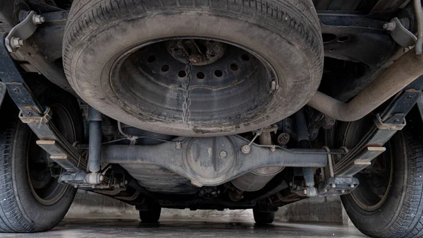 Maintenance background of car's suspension reveals the rear drive shaft. Cars parked on the cement floor.